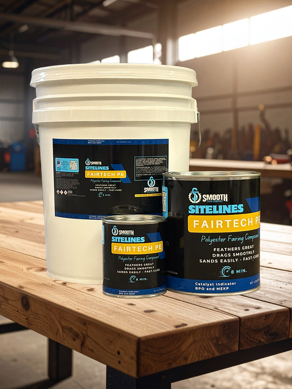 Three cans of Sitelines Fairtech polyester fairing compound on a wooden table in an industrial setting